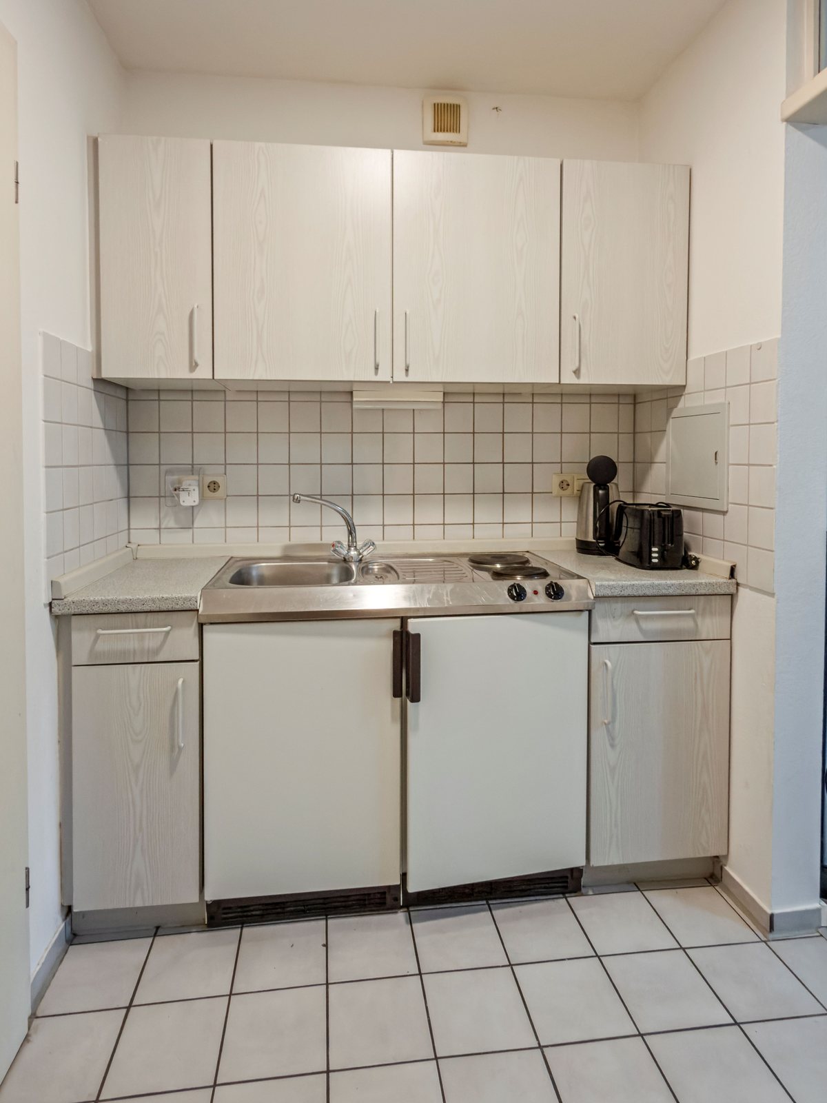 Küchenzeile mit Spüle, zwei Kochplatten, Wasserkocher und Toaster sowie Ober- und Unterschränken